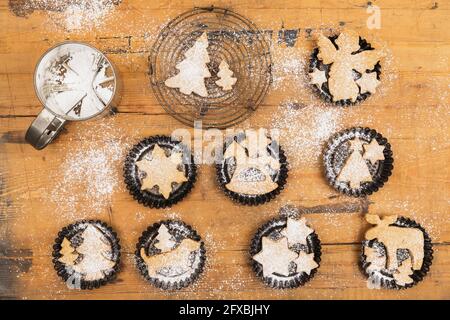 Shaker di zucchero in polvere e biscotti freschi fatti in casa di Natale sdraiati su una superficie di legno Foto Stock