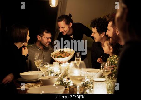 Sorridendo uomini e donne che guardano la pasta tenuta dall'uomo maturo in cucina Foto Stock