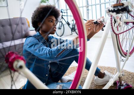 Donna concentrata con afro hairstyle riparando la bicicletta a casa Foto Stock