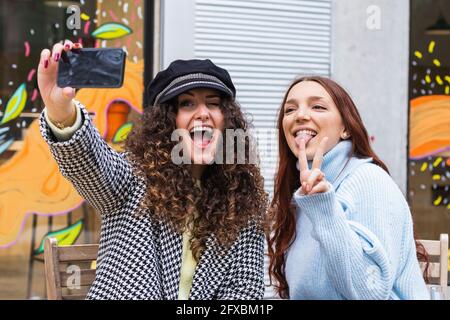 Amici giovani allegri che prendono selfie attraverso il telefono cellulare al bar Sidewalk Foto Stock