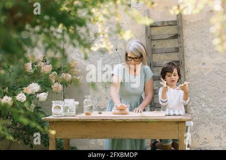 Nipote che gioca con l'impasto mentre la nonna impastava l'impasto nel cortile posteriore Foto Stock