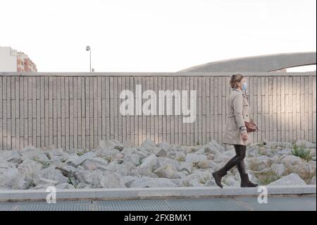 Bella ed elegante donna di mezza età con una maschera a piedi attraverso la città con un muro di mattoni e pietre dentro lo sfondo Foto Stock