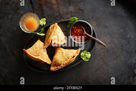 Vassoio con gnocchi di samosa, ciotola di salsa al peperoncino e bicchiere di tè chai Foto Stock
