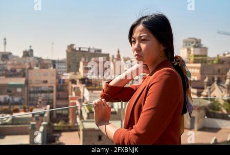 Donna premurosa che guarda alla vista mentre si alza sulla terrazza dell'edificio Foto Stock