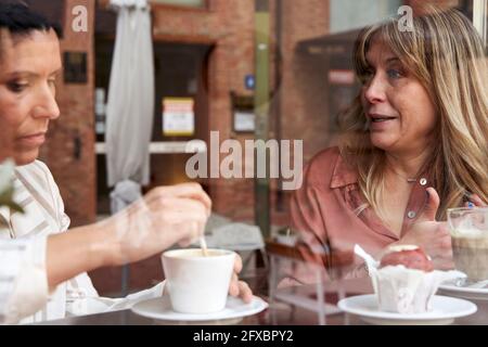 Amici femminili che chiacchierano mentre si beve un caffè in caffetteria visto attraverso il vetro Foto Stock