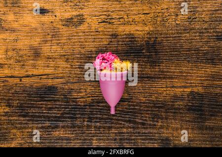 Coppa mestruale con fiori su sfondo di legno Foto Stock