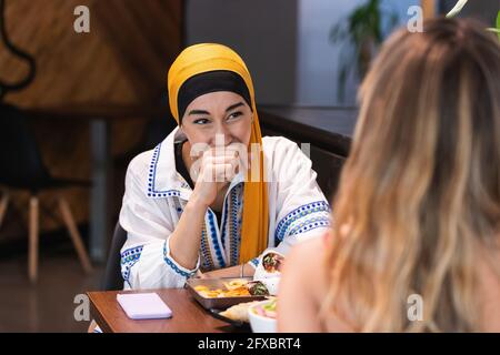 Giovane donna allegra che guarda l'amica seduto in ristorante Foto Stock