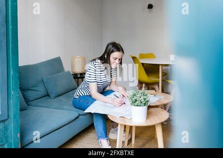 Donna che scrive sul giornale in appartamento Foto Stock