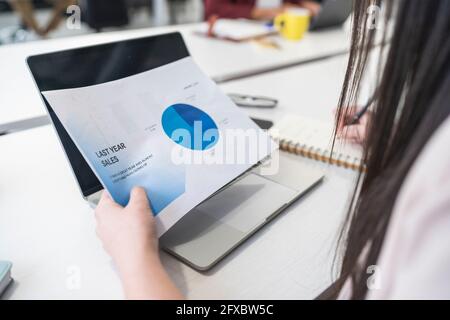 Donna d'affari che analizza i dati di vendita in ufficio Foto Stock