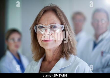 Donna dottore che indossa occhiali protettivi con colleghi in background in ospedale Foto Stock