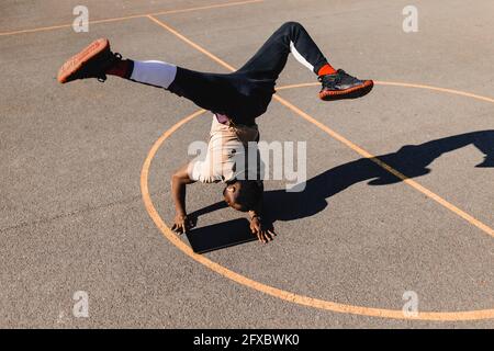 Giovane uomo che si bilancia con il supporto a mano utilizzando il tablet grafico sul campo da pallacanestro durante la giornata di sole Foto Stock