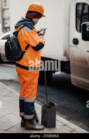 Urban Street operaio ragazza pulitore in tute luminose con attenzione e interesse con lo smartphone Foto Stock