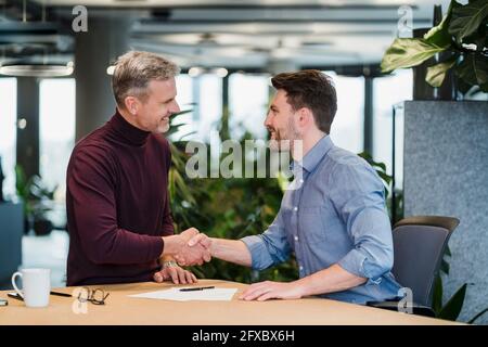 Sorridente gente d'affari che scuote le mani sul posto di lavoro Foto Stock