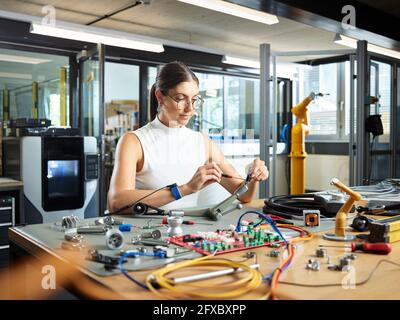 Ingegnere femminile che lavora con componenti elettrici nell'industria Foto Stock