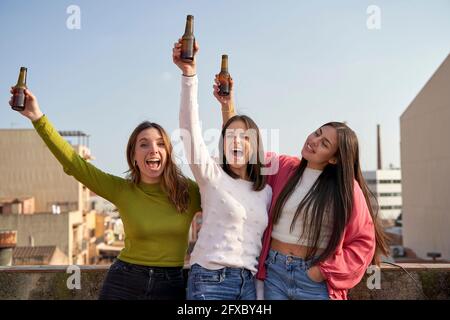 Felici le amiche che alzano le bottiglie di birra godendosi sul tetto Foto Stock