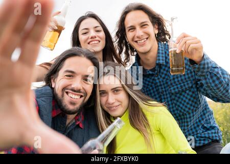 Felici amici che mostrano bottiglie di birra di fronte al cielo Foto Stock