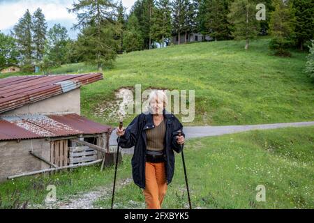 Donna che cammina sull'erba mentre tiene il palo escursionistico in provincia di Brescia, Lombardia, Italia Foto Stock