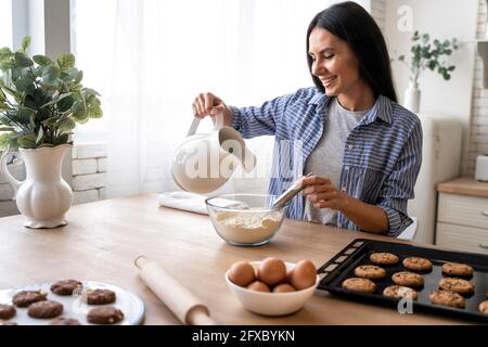 Donna che versa acqua nella farina mentre prepara il cibo in cucina a casa Foto Stock