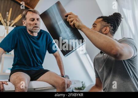 Fisioterapista che discute l'immagine radiografica del ginocchio con il paziente di sesso maschile Foto Stock