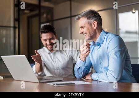 Sorridenti professionisti maschi che parlano di un computer portatile nella sala riunioni Foto Stock