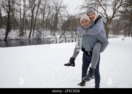 Uomo piggybacking giocosa donna mentre in piedi sulla neve Foto Stock