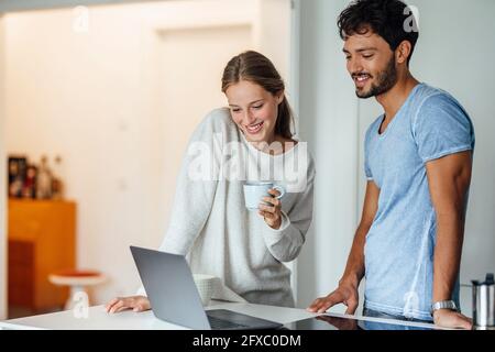 Donna felice che guarda il notebook mentre si è in piedi da ragazzo a casa Foto Stock