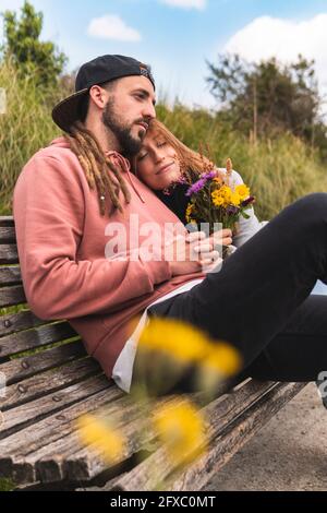 Giovane donna che si rilassa sulla spalla del ragazzo sulla panchina Foto Stock