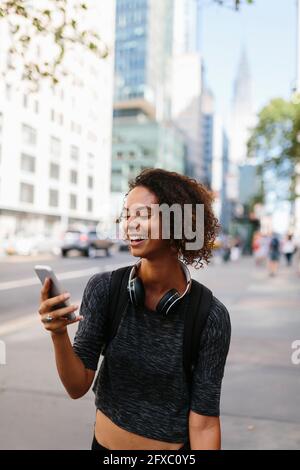 Donna con cuffie che utilizza smartphone in città Foto Stock