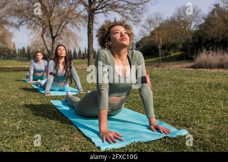 Le giovani donne che fanno la posizione verso l'alto del cane nel parco pubblico durante la giornata di sole Foto Stock