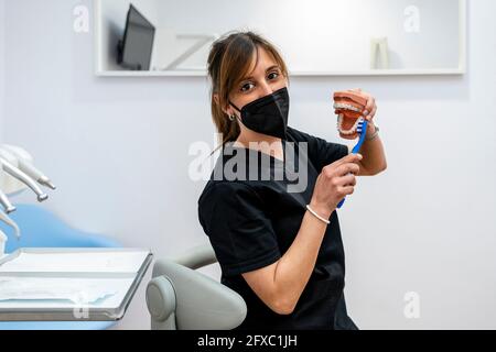 Dentista femminile spazzolando muffa dentale durante la pandemia presso la clinica medica Foto Stock