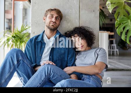 Una coppia stanca appoggiata sulla colonna mentre si siede sul pavimento dell'appartamento di casa Foto Stock