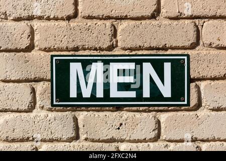 Fotografia di un segno di gabinetto da uomo in metallo bianco e nero su una parete di mattoni marrone chiaro al sole Foto Stock