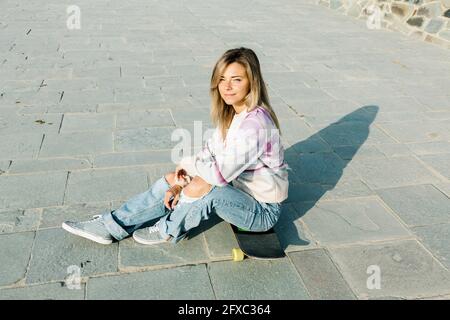 Donna bionda seduta sullo skateboard durante il giorno di sole Foto Stock