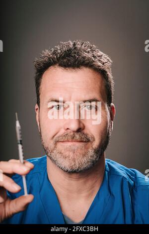 Medico maturo con siringa davanti a sfondo grigio Foto Stock