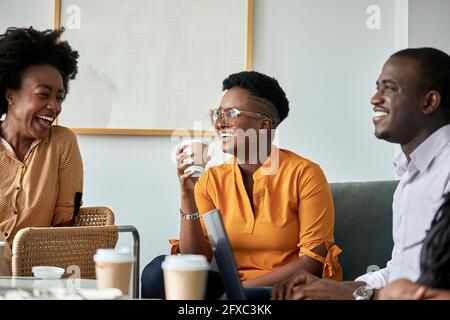 Felici professionisti di sesso maschile e femminile che discutono durante la pausa caffè in ufficio Foto Stock