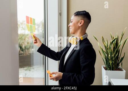 Donna d'affari sorridente che aderisce note adesive sulla finestra in ufficio Foto Stock