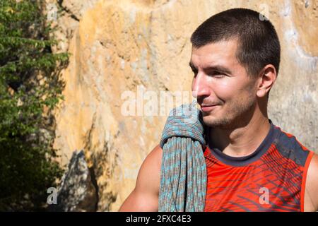 Un arrampicatore maschio di aspetto caucasico con una corda avvolta in mano. Avvolgimento della fune, nodo, stoccaggio delle attrezzature. Mano in magnesia bianca. Rosso sport Jerse Foto Stock