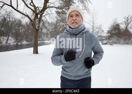 Uomo anziano che indossa abiti caldi che corrono al parco Foto Stock