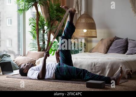 Giovane uomo africano sportivo che lavora a casa, si riscalda usando la cintura yogic Foto Stock