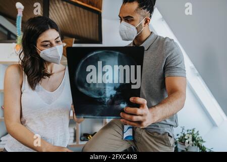 Fisioterapista maschile che discute l'immagine radiografica del collo e della testa con la paziente femminile nella pratica durante la pandemia Foto Stock