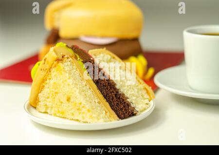 Pezzo della torta Burger, Madeira e torta stratificata di spugna di cioccolato, riempito con glassa ricoperta di glassa morbida e decorazioni di zucchero commestibile, torta i Foto Stock