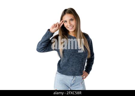 Bella donna latina che guarda avanti ondeggiando con la mano sulla fronte e con un atteggiamento felice su uno sfondo bianco puro. Foto Stock