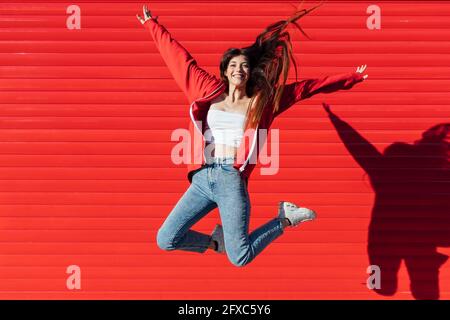 Ragazza adolescente con i capelli mozled che saltano davanti alla parete rossa Foto Stock