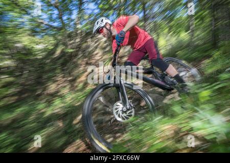Atleta maschile che si sposta in giù mentre si guida in bicicletta nella foresta Foto Stock