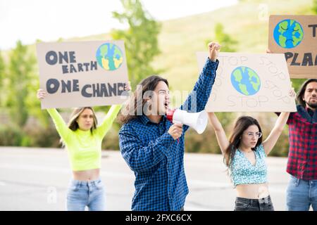 Attivista maschile con megafono che annuncia il cambiamento climatico con i manifestanti in background sul sentiero Foto Stock