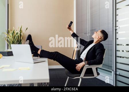 Donna d'affari sorridente che prende selfie attraverso il telefono cellulare in ufficio Foto Stock