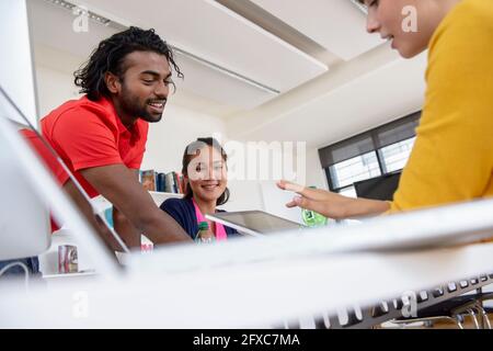 Studenti internazionali di sesso maschile e femminile che discutono su tablet digitale in biblioteca Foto Stock