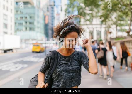 Donna felice con i capelli tosati che ascolta la musica sulle cuffie in città Foto Stock