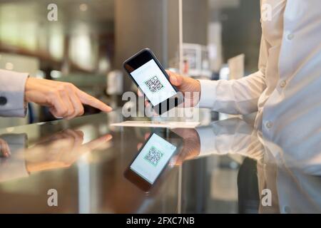 Receptionist femminile che indica il codice QR scansionato dal cliente maschile alla scrivania Foto Stock