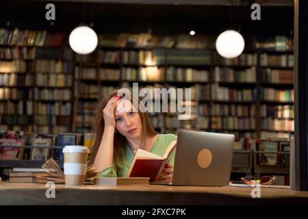 Studentessa che tiene un libro in biblioteca Foto Stock